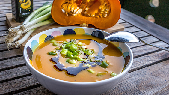 Kürbissuppe mit Kürbiskernöl in einer Suppenschüssel und einem aufgeschnittenen Hokkaido-Kürbis