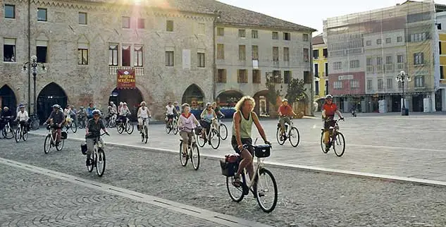 Das Bild zeigt eine Gruppe von Radfahrern, die durch die Piazza Maggiore in Este, Italien, fahren